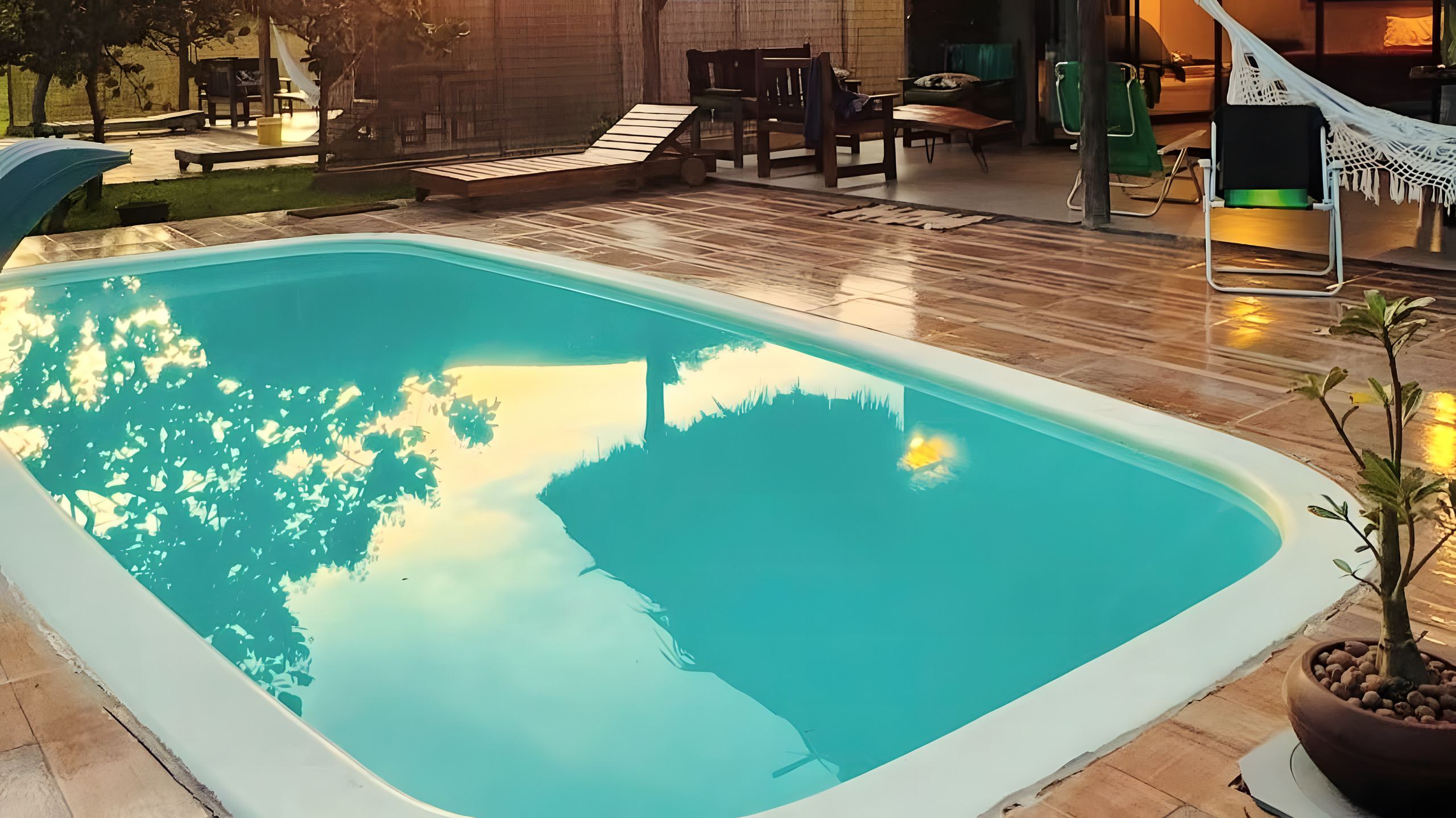 A piscina privativa do chalé no fim da tarde, com a varanda, a rede e as espreguiçadeiras de madeira