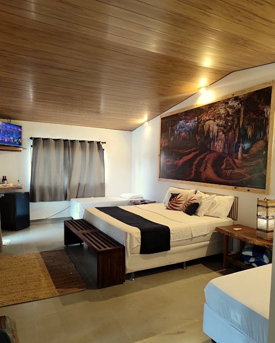 Quarto do chalé com teto de madeira, cama de casal e um painel gigante de foto de caverna na parede